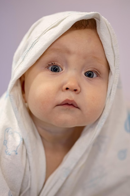 Het mooie babymeisje bedekt met een handdoek zit te wachten op de ouder