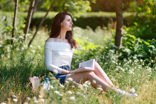 Het mooie jonge meisje leest in openlucht een boek in een de zomerpark.