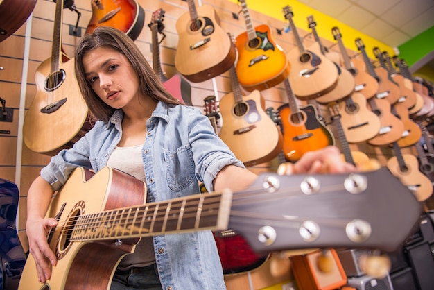 Het mooie jonge meisje speelt gitaar in een muziekopslag.