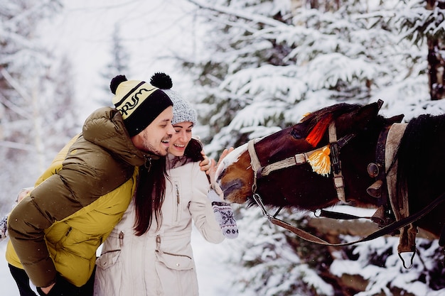 Het mooie jonge paar in de winter strijkt een paard