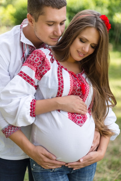 Het mooie jonge zwangere paar kleedde zich in nationale Oekraïense stijl in de herfstpark. Moederschap en gezinsgeluk concept.