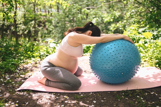 Het mooie jonge zwangere vrouw doen die met geschiktheid pilates blauwe bal in park uitoefenen openlucht