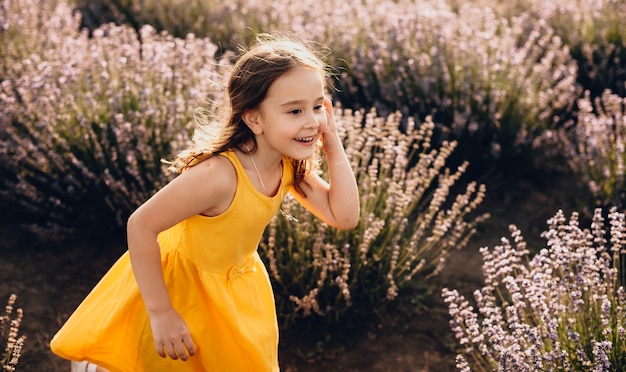 Het mooie Kaukasische meisje dat een gele kleding draagt, speelt vreugdevol met haar haar in een lavendelgebied