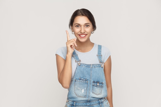 Het mooie latijnse meisje kreeg het idee en ze stak haar vinger op. geïsoleerde studio-opname op grijze achtergrond