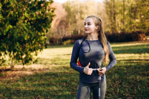 Het mooie meisje in het de herfstpark meet haar taille, weg kijkend.