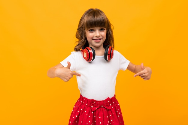 Het mooie meisje in kleding luistert aan muziek die op geel of oranje wordt geïsoleerd