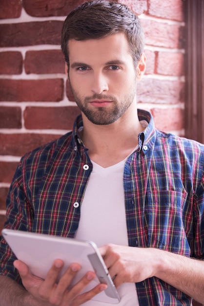 Het onderzoeken van zijn gloednieuwe tablet. Knappe jonge man die een digitale tablet vasthoudt en naar de camera kijkt terwijl hij binnenshuis staat