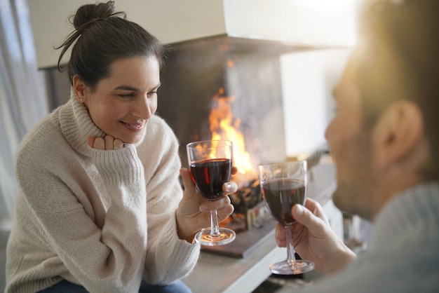 Het ontspannen van het paar door de brand die van glas rode wijn geniet