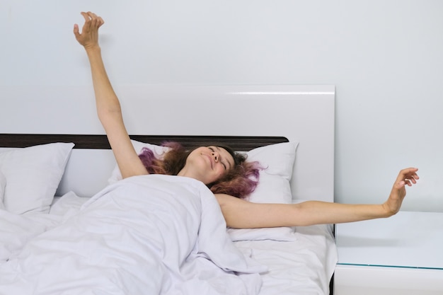 Het ontwaken van het tienermeisje in de ochtend liggend op hoofdkussen in bed met open wapens