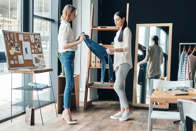 het ontwikkelen van een nieuwe modellijn. volledige lengte van mooie jonge vrouwen die jeans vasthouden en ernaar kijken