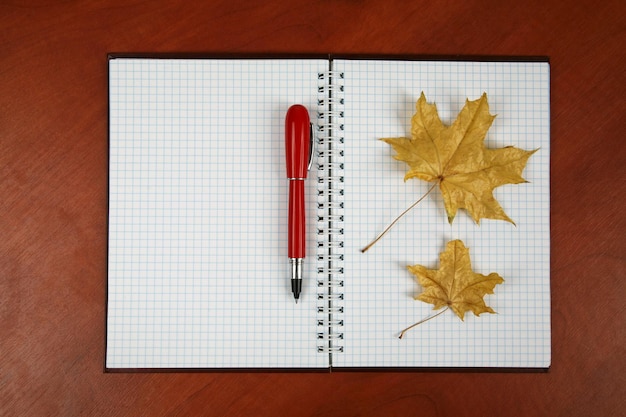 Het open notitieboekje en de rode pen met herfstblad liggend op een houten tafel