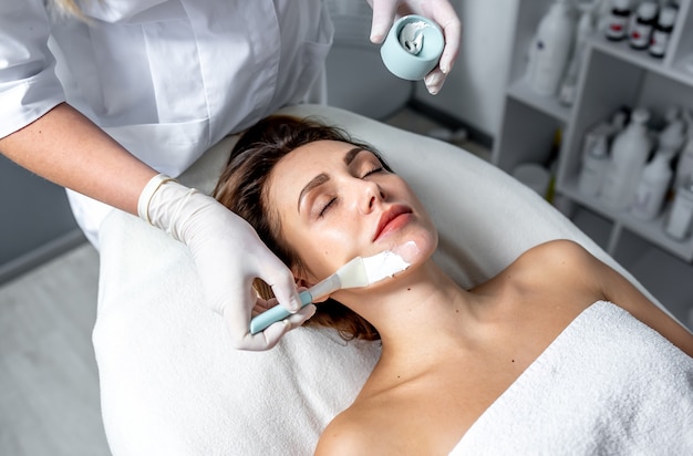 Het opleggen van een cosmetisch masker op het gezicht. Een schoonheidsspecialist-dermatoloog in een cosmetische kliniek.