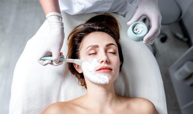 Het opleggen van een cosmetisch masker op het gezicht. Een schoonheidsspecialist-dermatoloog in een cosmetische kliniek.