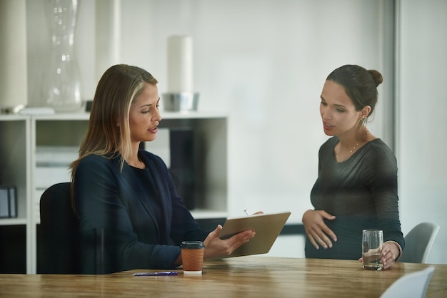 Het oversteken van de T's voordat haar vertrek begint Shot van een zwangere zakenvrouw en een collega die samen een digitale tablet gebruiken in een kantoor