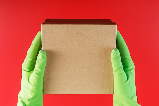 Foto het pakket van de bezorgdienst in de handen met groene rubberen handschoenen op een rode achtergrond.