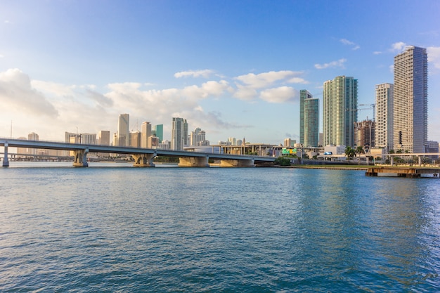 Het panorama van de de stadshorizon van Miami bij bewolkte blauwe hemel en brug over overzees met bezinning