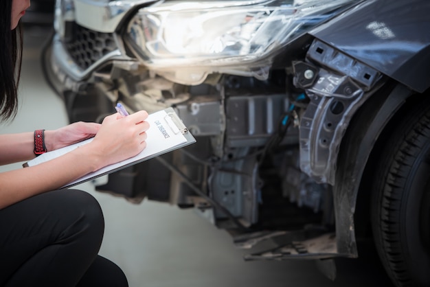 Het personeel van de verzekeringsagent schrijft op het klembord terwijl het de auto controleert na te zijn geëvalueerd en vervolgens het ongeval heeft geclaimd - de auto heeft een ongevallenverzekering.