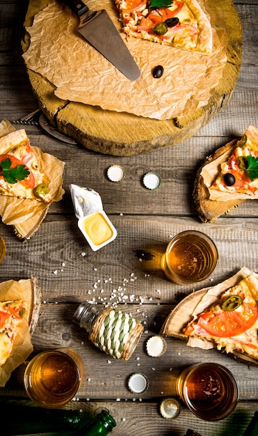 Het pizzaparty. pizza en bier voor vier personen. op een houten tafel. bovenaanzicht