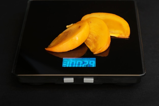 Het plakje persimmon staat op een elektronisch gewicht op een zwarte achtergrond.