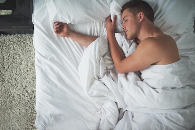 Het plezier van slapen Bijgesneden opname van een shirtloze jonge man die in zijn slaapkamer slaapt