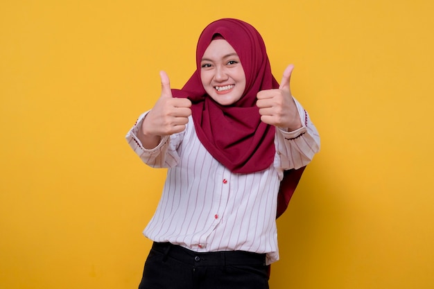 Het portret van de aziatische jonge vrouw die hijab draagt, geeft twee duimen en kijkt gelukkig uitdrukking