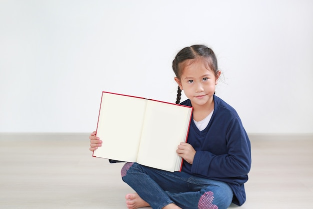 Het portret van de Aziatische meisjeszitting in kamer met open boek toont lege pagina