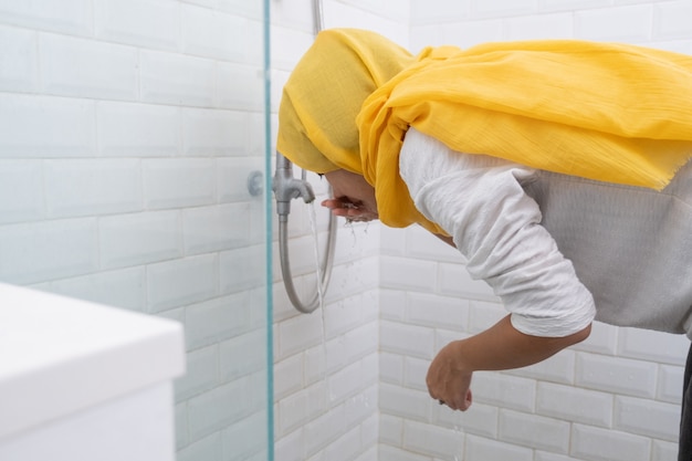 Het portret van de jonge moslimvrouw voert thuis wassing (wudhu) uit vóór gebed