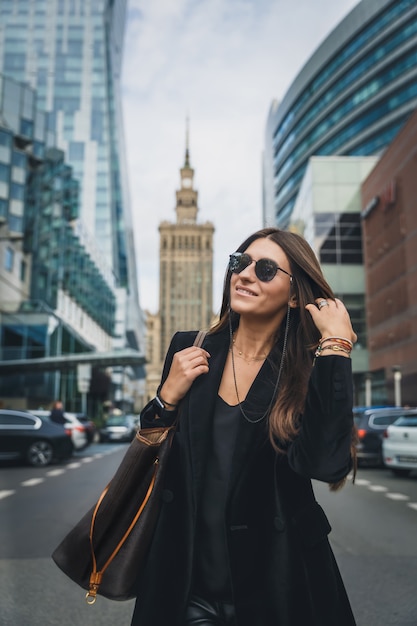 Het portret van de maniervrouw van het jonge vrij trendy meisje stellen bij de stad in Europa.