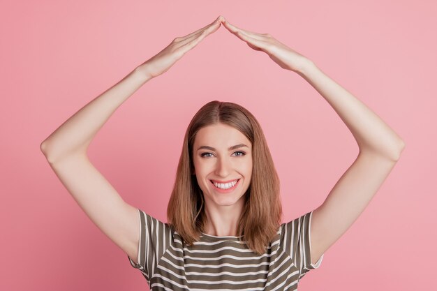 Het portret van de positieve vrolijke handen van de dameagent maakt dakgebaar op roze achtergrond