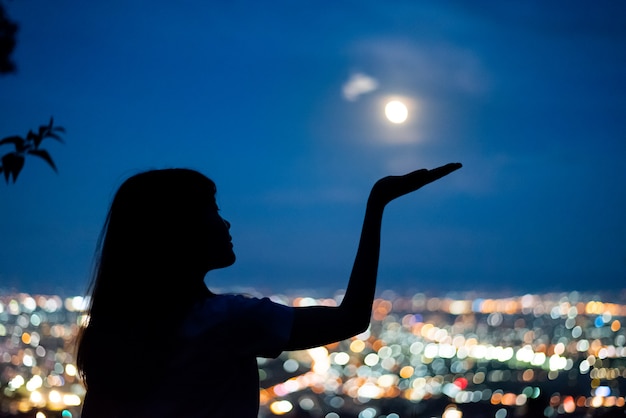 Het portret van de silhouetvrouw met volle maan op lichte bokehachtergrond van de stadsnacht, Chiang-MAI, Thailand