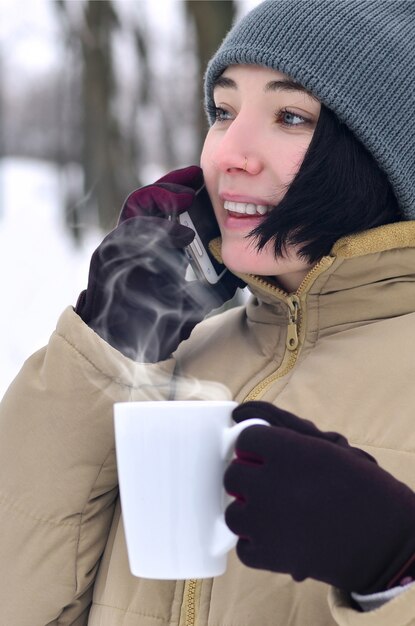 Foto het portret van de winter van jong meisje met smartphone en koffiekop