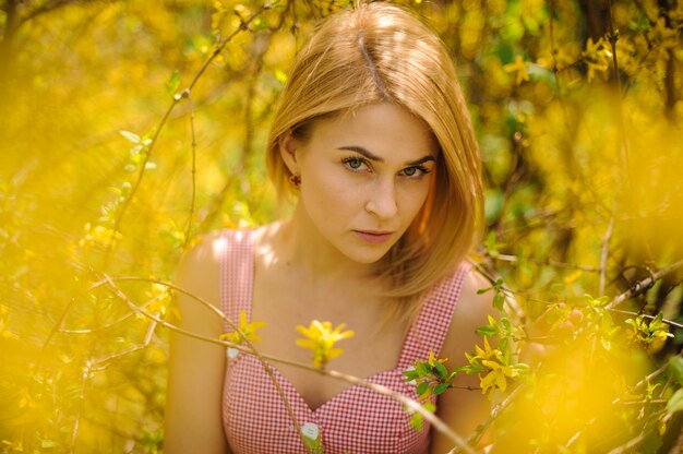 Het portret van een jonge blonde vrouw kleedde zich in een roze kleding die zich dichtbij de gele bloeiende boom bevinden