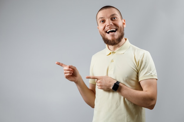 Het portret van een jonge man in een geel T-shirt toont aan de kant op grijs.