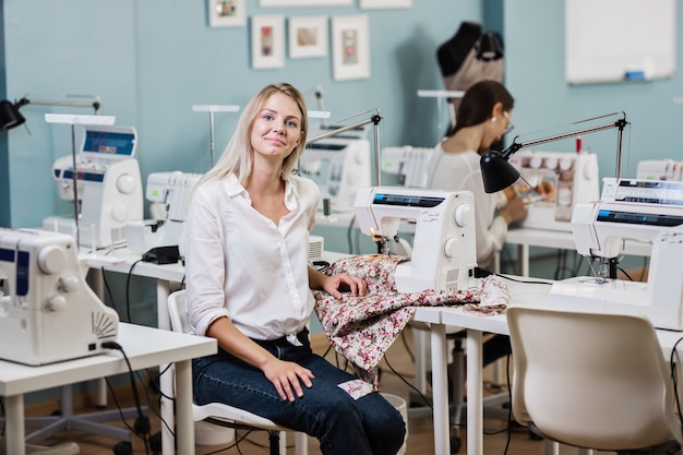 Het portret van een mooie blonde vrouw met een wit overhemd naait met de elektrische naaimachine