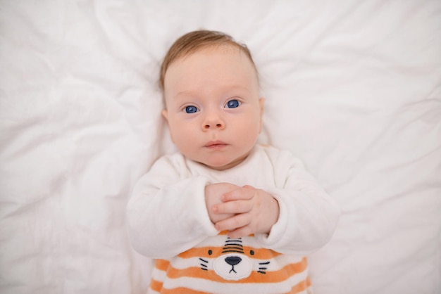 Het portret van een schattig drie maanden oude baby gekleed gele bodysuit ligt op de witte deken
