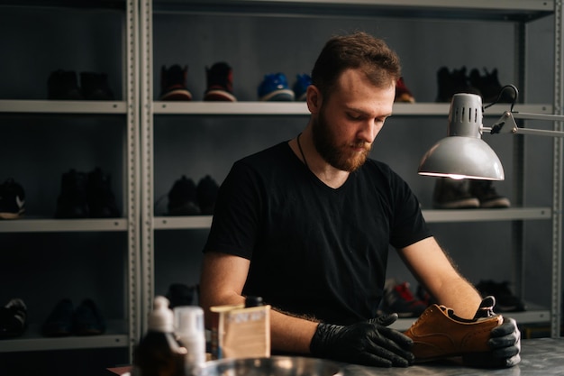 Het portret van een schoenmaker die zwarte handschoenen draagt, steekt een houten schoenkussen in versleten lichtbruine leren schoenen om gerepareerd te worden in een donkere ambachtelijke schoenenwinkel. concept van schoenmaker ambachtelijk werk.