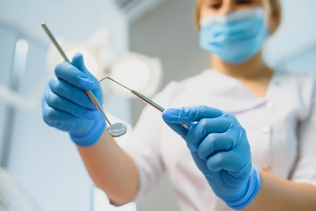 Het portret van een tandarts die tandheelkundige instrumenten in zijn handen houdt in de kliniekclose-up