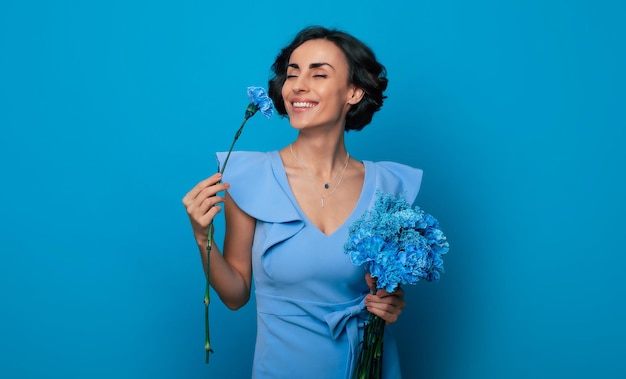 Het portret van een vrolijke opgewonden prachtige jonge vrouw in een elegante blauwe jurk poseert met een verse bos blauwe bloemen. Moederdag. Vrouwen vakantie. Lente. Vrouwenrechten