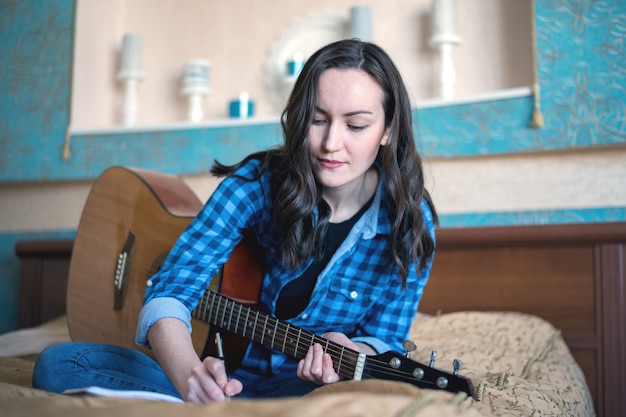 Het portret van een vrouw maakt muziek met een akoestische gitaar het schrijven ideeën in een notitieboekje