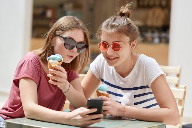 Het portret van gelukkige tieners bekijkt foto's in sociale netwerken via celtelefoon