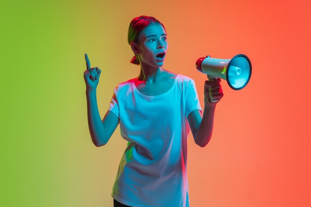 Het portret van het jonge kaukasische meisje op de achtergrond van de gradiëntgroen-oranje studio in neonlicht