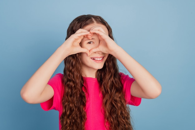 Het portret van het romantische charmante meisje toont het symbool van het liefdehartgebaar op blauwe achtergrond