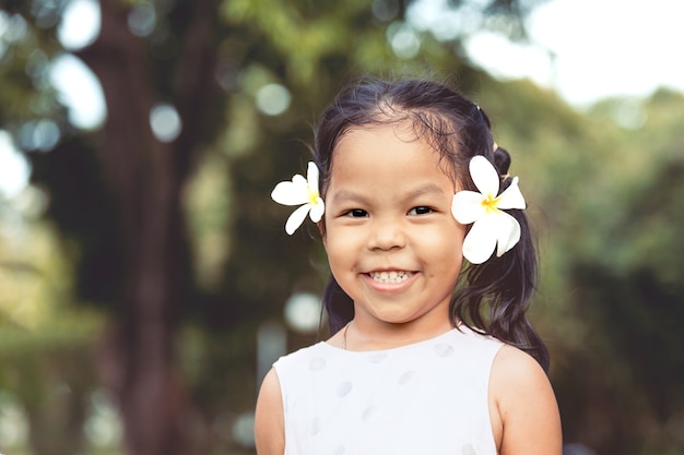 Het portret van leuk Aziatisch kindmeisje met bloem op haar oren glimlacht met gelukkig in het park in uitstekende kleurentoon