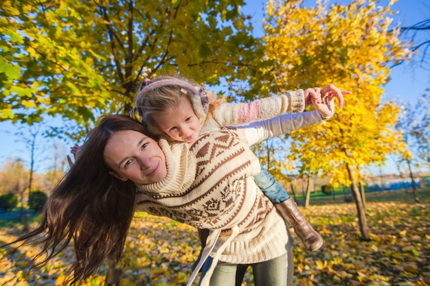 Het portret van leuk meisje en gelukkige moeder hebben pret in geel de herfstbos op een warme zonnige dag