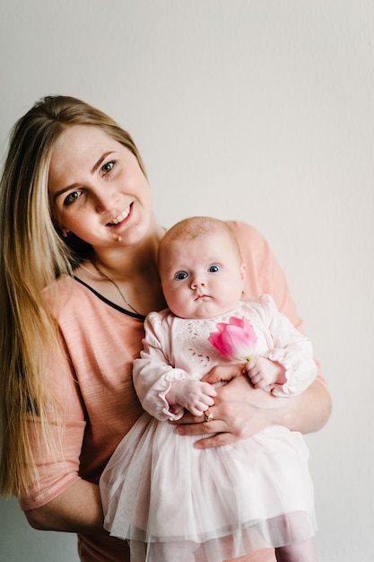 Het portret van mamma houdt klein babymeisje met bloem roze tulp op een lichte achtergrond. Nieuw leven, liefde en vakantieconcept. Vrouwendag. Moederdag.