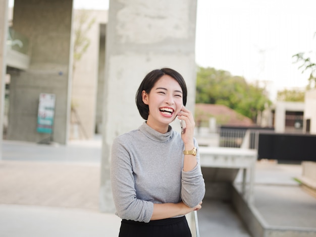 Het portret van Mooie Aziatische vrouw die mobiele telefoon in jonge bedrijfsvrouw met behulp van ziet eruit