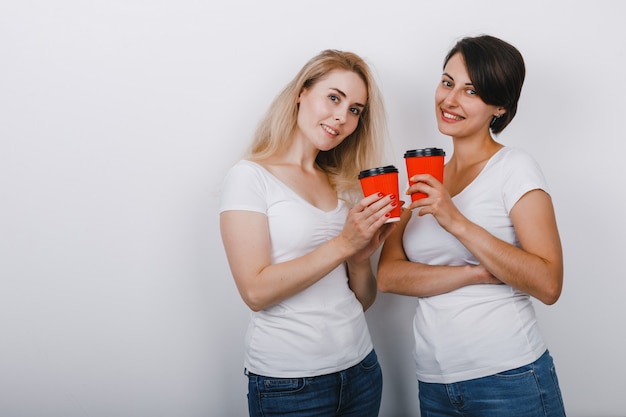 Het portret van twee vrouwenvrienden hief glazen koffie op en bekijkend zacht de camera