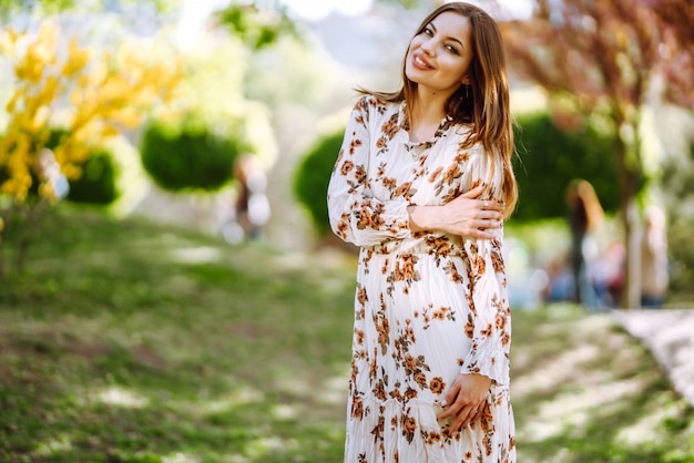 Het portret van vrouw in een mooie kleding met bloemen geniet van bloeiende groene tuin in de lentedag. Mode en stijl concept.