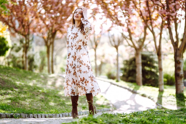 Het portret van vrouw in een mooie kleding met bloemen geniet van bloeiende groene tuin in de lentedag. Mode en stijl concept.