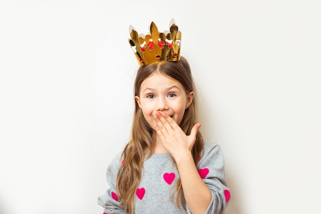 Het positieve kindmeisje met een kroon behandelt verlegen haar mond